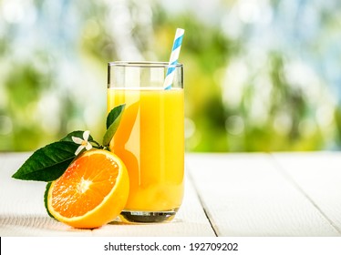 Tall glass of tasty freshly squeezed orange juice standing on an outdoor wooden picnic table on a hot summer day with a halved fresh orange - Powered by Shutterstock