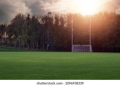 Tall goal post for Irish National sports on a training pitch against dark trees at sunset. Sun flare. Copy space. Camogie, hurling, rugby and Gaelic football playground. Calm mood.