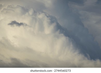 Tall and imposing wall clouds form around a large thunderstorm. Shadows and highlights emphasize the scale and massive size of the weather system. Rain and heavy winds accompany the towering clouds. Convective activity