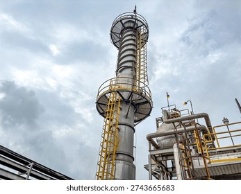 A tall industrial processing column with ladders and platforms against a cloudy sky, representing modern manufacturing and energy production.