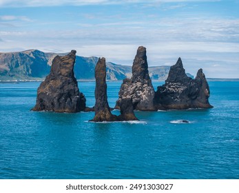 Tall, jagged black rock formations eroded by the sea stand in stark contrast to the calm blue ocean and sky, creating a stunning natural scene in Iceland. - Powered by Shutterstock