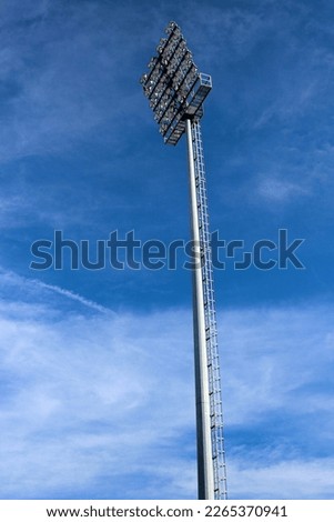 Tall lamp post, stadium light or sports lighting against blue sky background