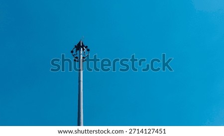 Tall lighting tower with multiple floodlights standing against a clear blue sky. Minimal urban infrastructure scene, modern technology, outdoor daylight, strong vertical composition