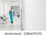 A tall male doctor with a beard walks along the hospital corridor with a folder of documents and enters his office