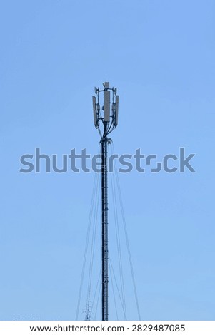 A tall metal cellular network tower equipped with multiple transmitters and transmitter antennas stands against a clear blue sky.