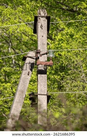 A tall pole with a wooden box on top of it. The pole is covered in rust and has a wire running down it. The box is old and has a few screws missing. The wire is tangled