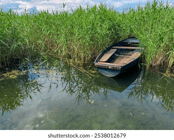 Tall reeds frame a rustic wooden boat floating on idyllic Lake Ohrid, North Macedonia. Calm waters reflect the cloudy sky and distant mountains and hills. Sense of solitude, tranquility and mystery. - Powered by Shutterstock