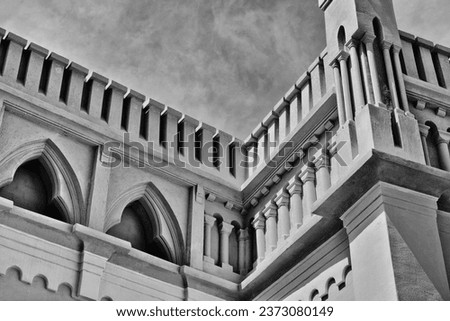tall retro stone castle or fort wall closeup. turret, stylish arched  openings. arrowslits. low angle view. concrete and stone masonry. corner tower. black and white image. light sky. black and white.