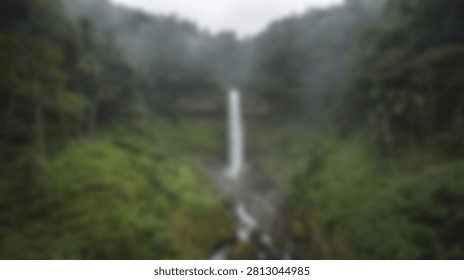 A tall, slender waterfall flows down a steep, densely forested mountainside covered in vibrant green moss and trees. The atmosphere is misty and serene.