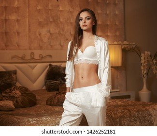 Tall Slim Eegant Woman In Expensive White Silk Pijamas Standing Near Bed In Luxury Apartments And Looking At You