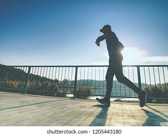 Tall slim man run on the lake terrace against the backdrop of a beautiful sunrise. Shore of mountain lake with dark forest hills - Shutterstock ID 1205443180