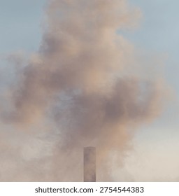 A tall smoke stack is spewing smoke into the sky. The smoke is white and gray. The sky is blue and clear