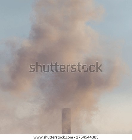 A tall smoke stack is spewing smoke into the sky. The smoke is white and gray. The sky is blue and clear