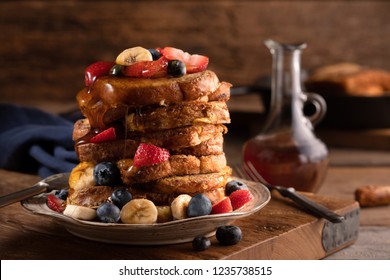 Tall stack of French toast covered with blueberries, strawberries, bananas and maple syrup in a rustic restaurant with a profile view in a horizonal format. - Powered by Shutterstock