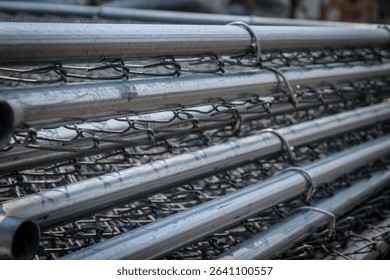 a tall stack of galvanized metal wire mesh fence panels ready for installation as a temporary barricade. industrial or construction design element or background