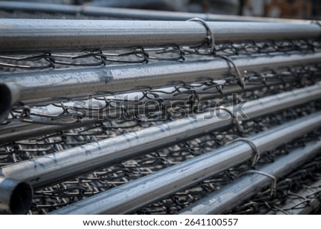 a tall stack of galvanized metal wire mesh fence panels ready for installation as a temporary barricade. industrial or construction design element or background