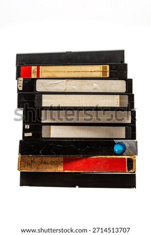 Tall stack of old black VHS video cassette tapes, some with red labels, isolated on white.