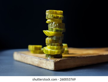 Tall Stack Of Pickle Chips On A Wooden Cutting Board. 