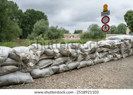 tall stack of sandbags forms a flood barrier along a riverbank. A 