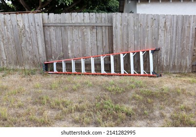 A Tall Step Ladder On The Ground Leaning Sideways Against An Old Fence.