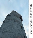 A tall, stone tower with a few small windows stands against a clear sky.