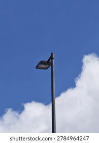 Tall streetlight pole with rectangular lamp fixture set against bright blue sky and scattered white clouds