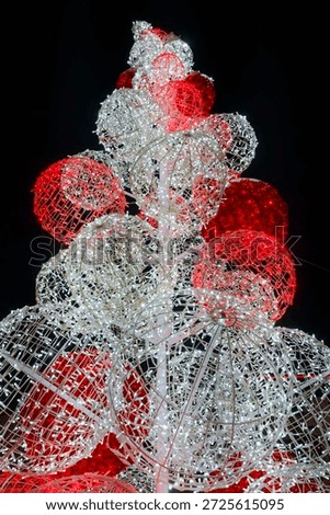A tall structure made of glowing wireframe spheres arranged to resemble a Christmas tree. The spheres are illuminated in shades of red and white against a dark night sky.