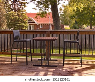 A tall table and two bar stools on a wooden back deck.