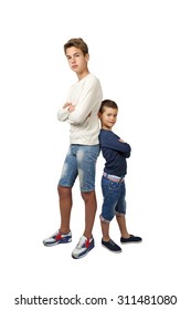 Tall teenager and little boy stand back to back with hands crossed on chest isolated on white background