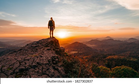 Tall tourist guide on rock. Hiker with sporty backpack stand on cliff above misty valley at sunset. Mountain meadow in spring or autumn. Vivid and strong vignetting effect. Horizontal, copy space