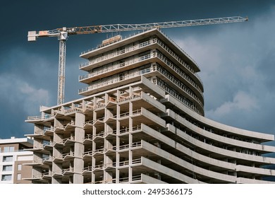 Tall tower crane above a huge skyscraper under construction against a stormy sky - Powered by Shutterstock