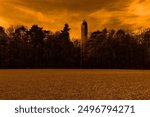 Tall tower in the forest, in the foreground plowed field, in the background of heaven with clouds, evening atmosphere, dark orange color