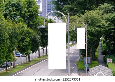 Tall vertical hanging blank advertising banners posters mockup; lush plants and tress in background; for OOH out of home lamp post media