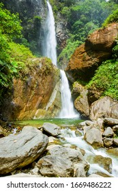 A tall waterfall flows down a steep, rocky cliff face into a clear green pool below, surrounded by lush green, Tungurahua Volcano, Pastaza River