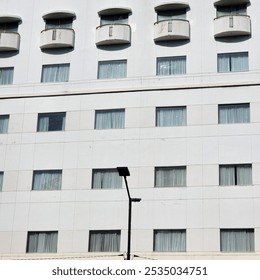 a tall, white building with many rectangular windows and balconies. There is a street lamp in front of the building.