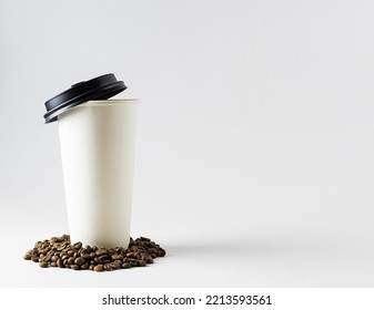 A Tall White Cardboard Coffee Cup With You On A White Table. Coffee Beans Are Covered In A Glass. White Background, Text Space