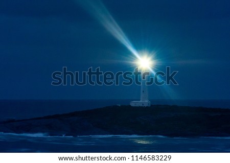 Tall white lighthouse at night with rays of light radiating out