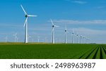 Tall wind turbines stand majestically against a vibrant sky, generating renewable energy amidst lush green fields in the Netherlands.