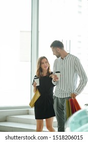 Tall Young Man With Cup Of Coffee Looking At His Pretty Girlfriend When They Are Walking In Shopping Mall