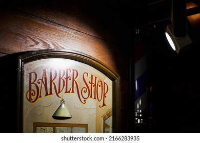 Tallinn, Estonia - 11.23.2021 - Vintage barbershop poster with BARBER SHOP text on wooden wall. Loft spotlight shines on wall banner wooden frame in barbershop interior, old stylish inscription