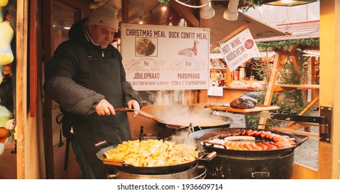 Tallinn, Estonia - December 22, 2017: Man Frying Potatoes And Sausages - A Traditional Christmas Dish Of Street Food On Streets Of Europe In Winter During The Christmas Holidays.