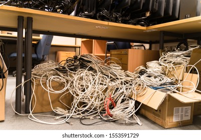 Tallinn / Estonia - November 07 2019:  Tangled Network Cables Gathered Into One Bunch During Clean Up. Liquidation Process Of The Business, Messy Cubicle Office. Red Rolled Wire Withing Grey Ones. 