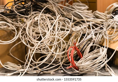 Tallinn / Estonia - November 07 2019:  Tangled Network Cables Gathered Into One Bunch During Clean Up. Liquidation Process Of The Business, Messy Cubicle Office. Red Rolled Wire Withing Grey Ones. 