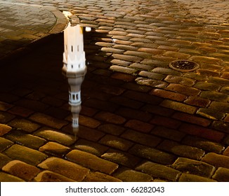 Tallinn town hall at night in Raekoya square showing the floodlit spire and tower of the hall reflected in a rain pool on the cobbled streets