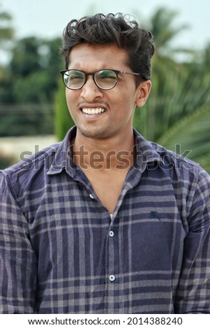 TALL,YOUNG,HANDSOME AND DUSKY SKINNED SOUTH INDIAN MALE WITH IDEAL SMILE AND SPECTACLES IN BLUE SHIRT