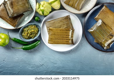 Tamale, traditional dish of the cuisine of Mexico, various stuffings wrapped in green leaves, top shot with copy space. Hispanic food. With chili peppers and tomatillos