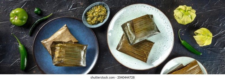 Tamales oaxaquenos panorama, traditional dish of the cuisine of Mexico, various stuffings wrapped in green leaves. Hispanic food. With chili peppers and tomatillos