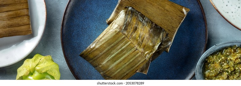 Tamales Overhead Flat Lay Panorama. Traditional Dish Of Mexican Cuisine, Various Stuffings Wrapped In Green Leaves. Hispanic Food. With Tomatillos And Salsa Verde