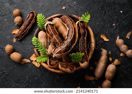 Tamarind tropical fruits with leaf in a wooden bowl. On a stone background.