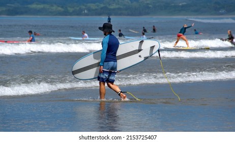 TAMARINDO, COSTA RICA - CIRCA NOVEMBER 2021: Person Walking On The Beach With A Surf Board